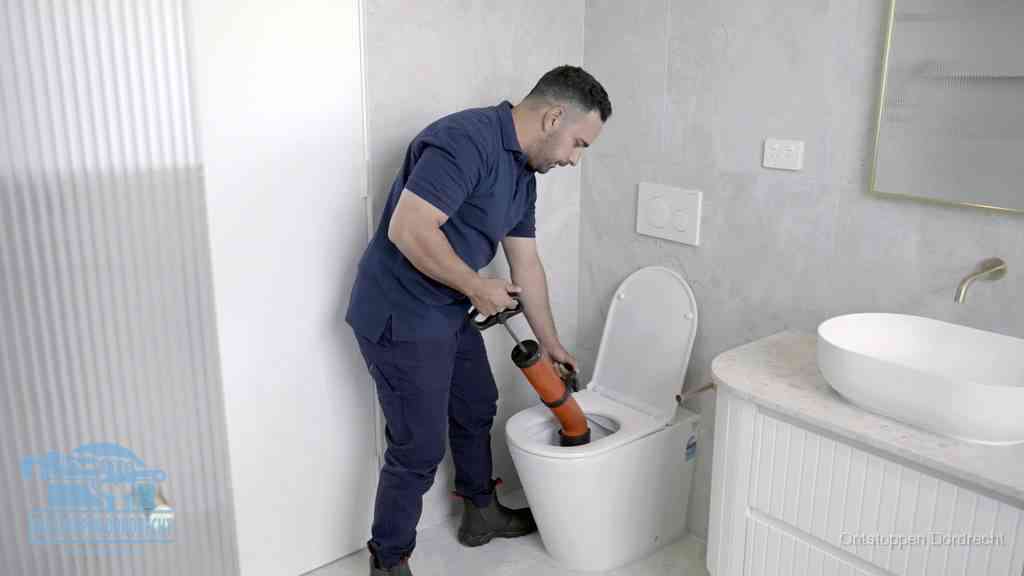 Een monteur buigt over een wandcloset en duwt met de hand een persluchtontstopper in de toiletpot om de verstopping handmatig los te maken in Dordrecht