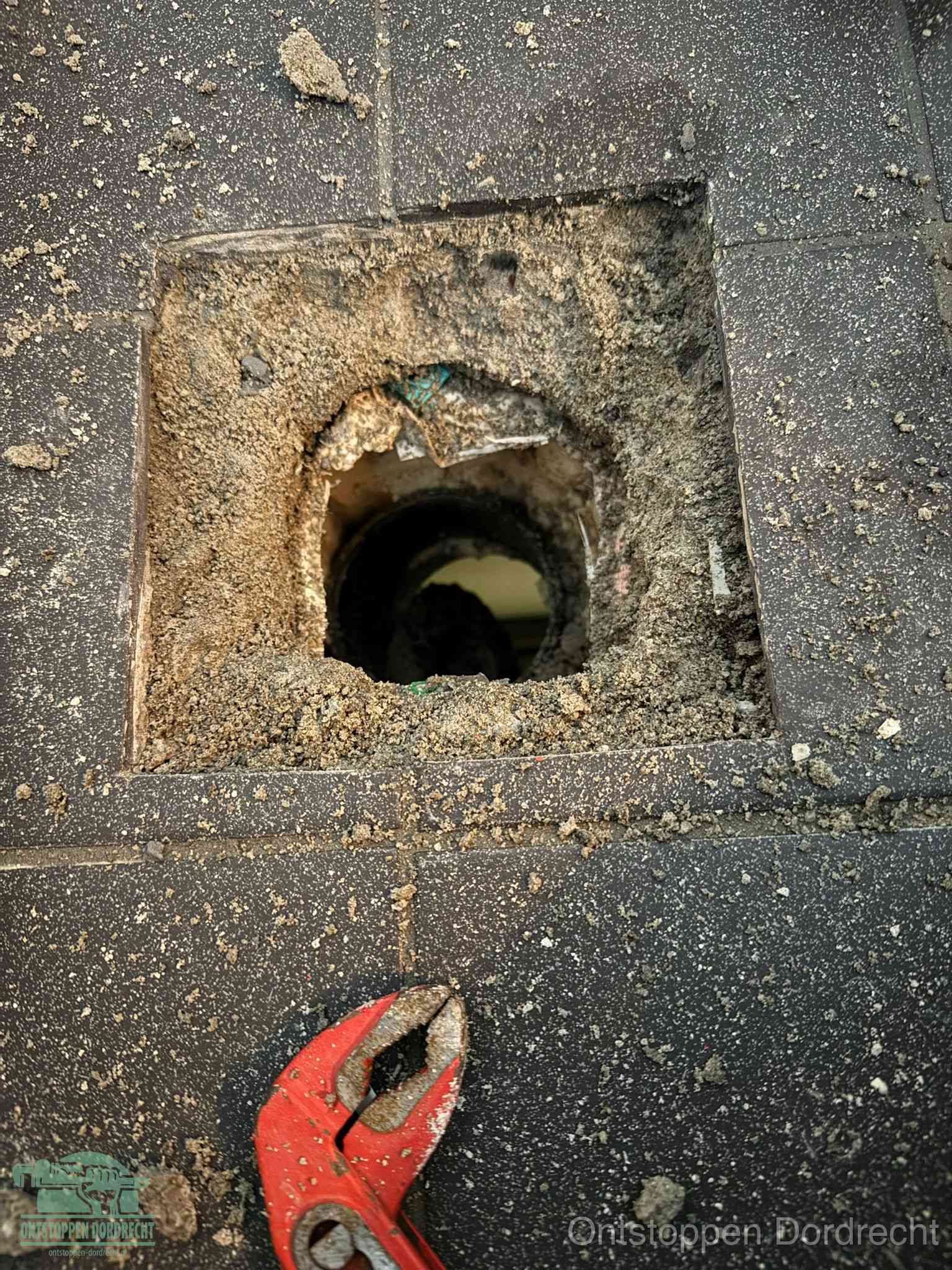 Een geopend rioolputje in een betontegelvloer met losgemaakt rooster en een zichtbare ronde afvoerbuis, het achterhalen waar de afvoerverstopping zit in Dordrecht