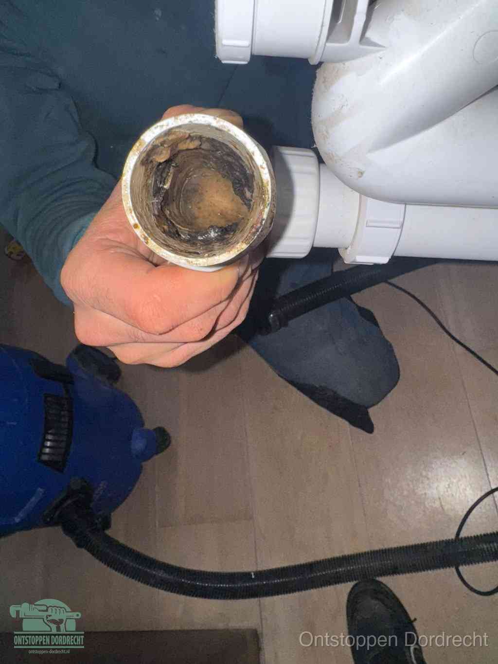 Een hand houdt een losgekoppeld PVC-afvoerbuisstuk vast dat van binnen volledig is dichtgeslibd met vet, vuil en aanslag, de meest voorkomende oorzaak van een verstopte afvoer in Dordrecht