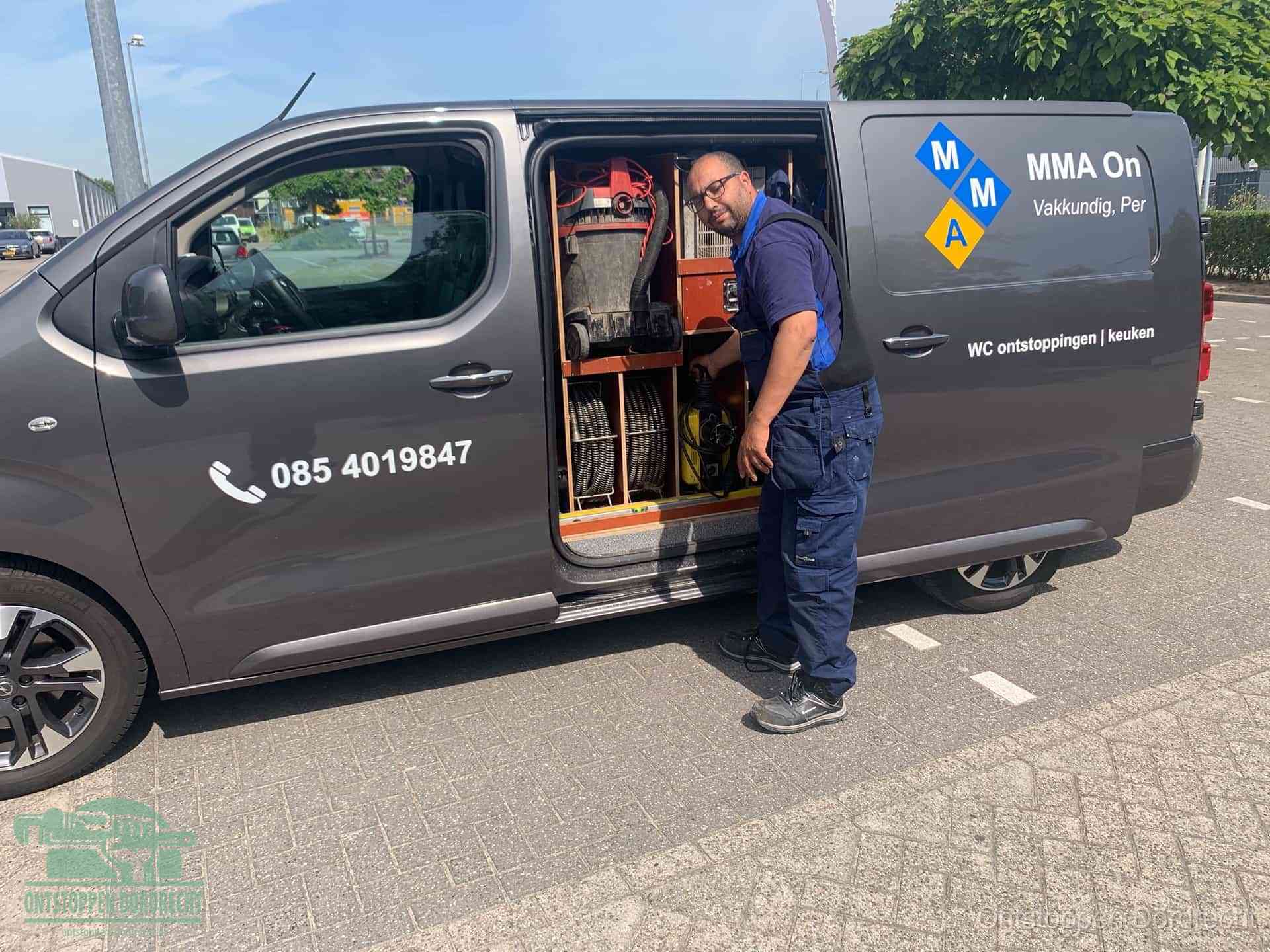 Een monteur bij de open schuifdeur van zijn bedrijfsbus op een parkeerplaats, klaar om de oorzaak van terugkerende afvoerverstoppingen aan te pakken in Dordrecht