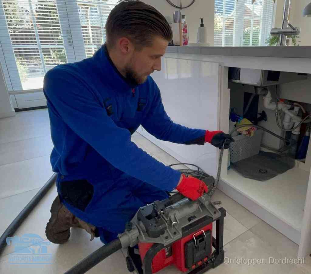 Een monteur voert een ontstoppingsveer in de keukenafvoer onder de spoelbak, waar ook de vaatwasser op aangesloten zit, in Dordrecht