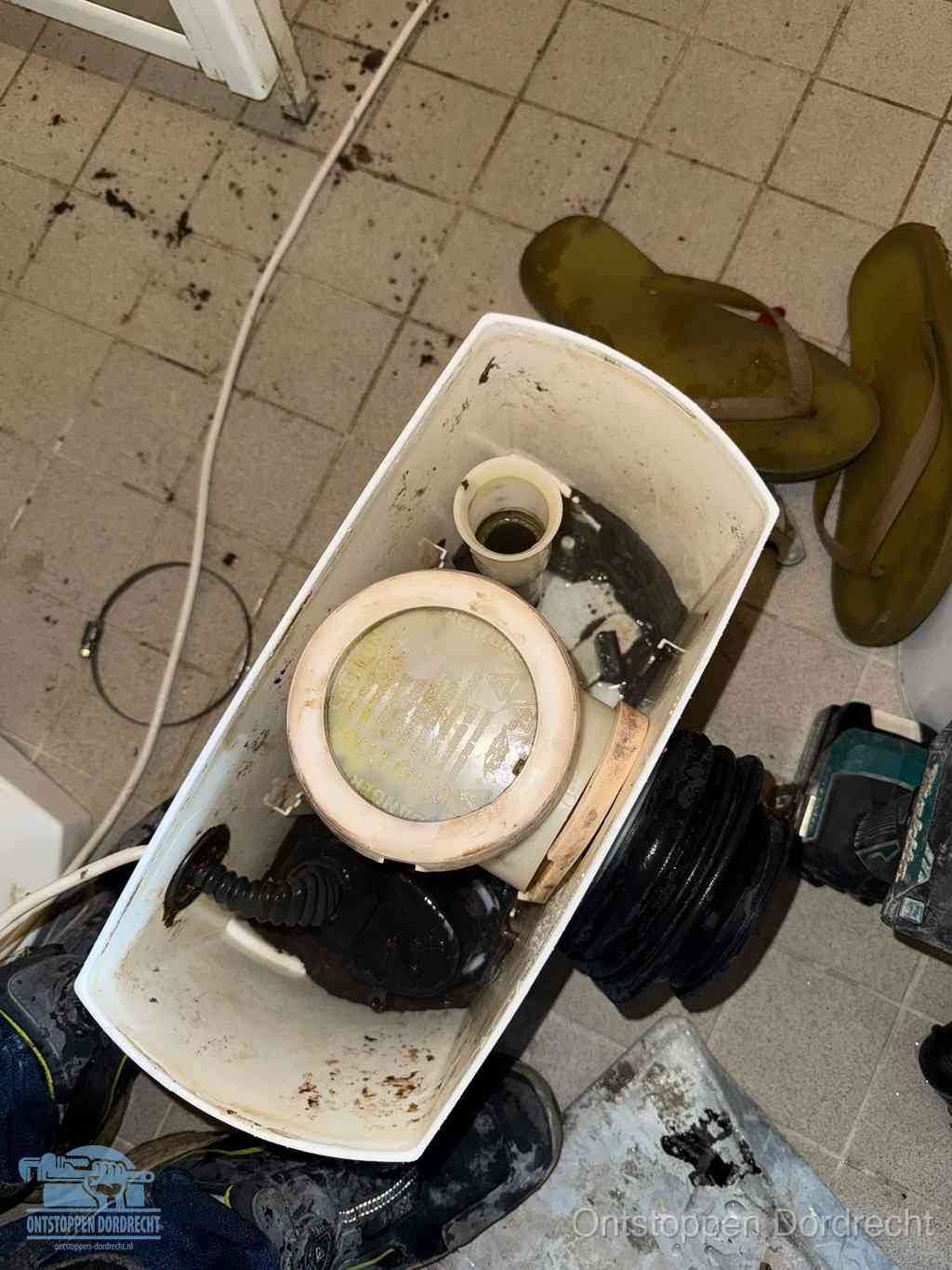 Een gedemonteerde toiletpot op de vloer met ontstoppingsveer en gereedschap ernaast, het verwijderen van een vastzittend voorwerp uit de wc in Dordrecht