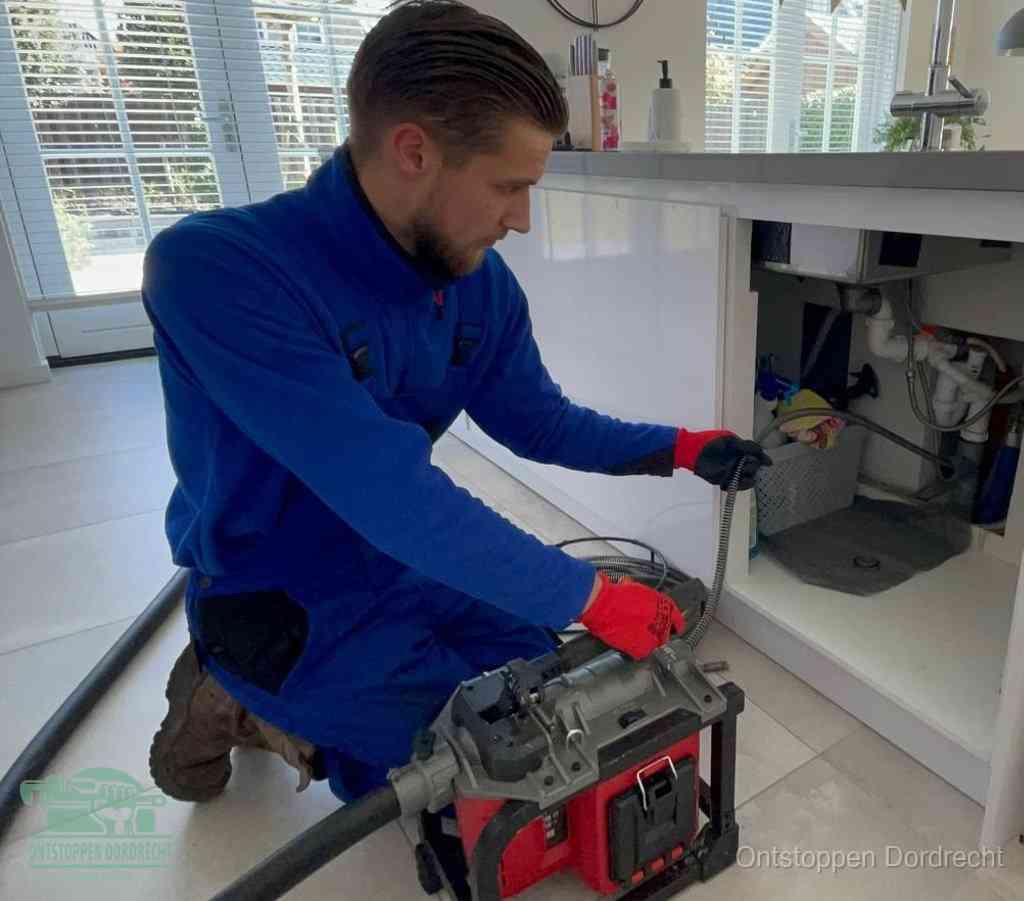 Een monteur met rode handschoenen knielt in een keuken en voert een elektrische ontstoppingsveer in tijdens het professioneel afvoer ontstoppen in Dordrecht