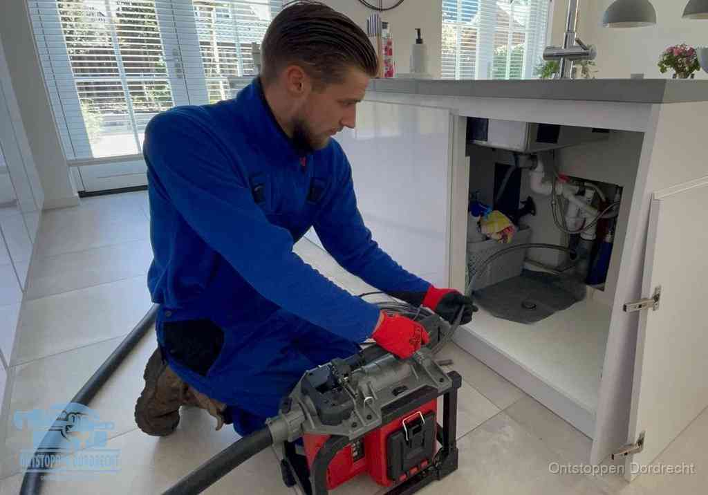 Een monteur voert een professionele elektrische ontstoppingsmachine in de afvoer onder de spoelbak tijdens het gootsteen ontstoppen in Dordrecht